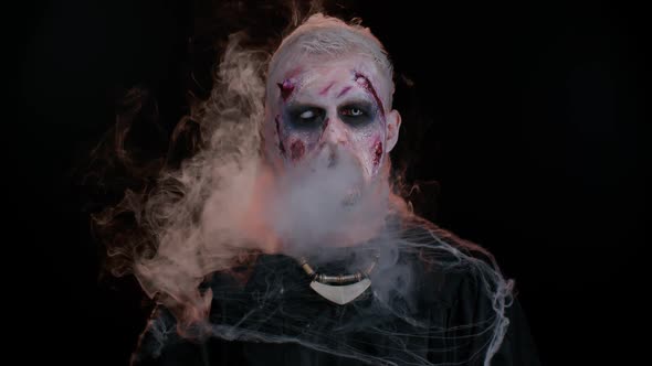 Frightening Man with Halloween Zombie Makeup Blows Smoke From Nose and Mouth Trying to Scare