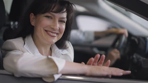 Happy Smiling Beautiful Woman Sitting on Passenger Seat in Car Looking at Camera with Blurred Man at
