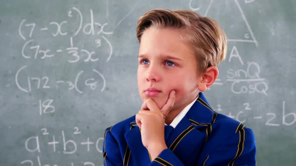 Thoughtful schoolboy standing in front of chalkboard