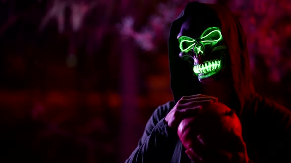 Portrait of a Person in a Terrible Glowing Mask of Death and in a Cape with a Hood Against the