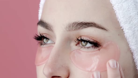 Plesant nude girl applying collagen eye masks on face in front of a mirror.