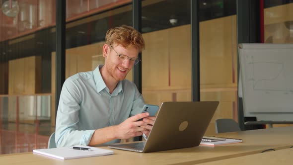 Smiling Young Adult European Businessman Using Mobile Phone in Office