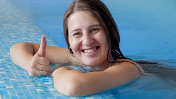 Portrait of Happy Cheerful Smiling Woman Relaxing in Swimming Pool and Showing Thumbs Up