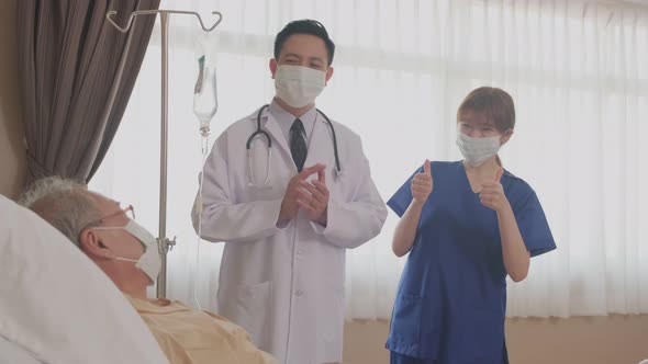 Asian happy doctor and nurse giving encourage to sick old man lying on bed by clapping the hands.