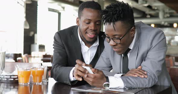 African Businessmen Friends Discussing Funny Photos Together on Smart Phone in Cafe