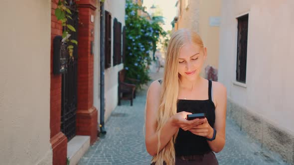 Pretty Blonde Girl Chatting on Smartphone While Walking Down the Street