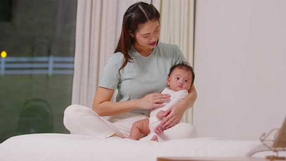 Beautiful Asian mom woman holding newborn baby in her arms sit on bed at white cozy home