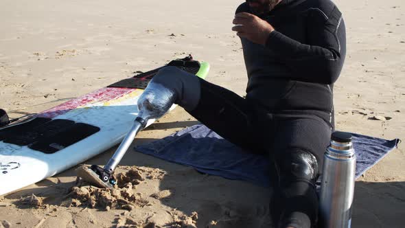 Quite Surfer with Disability Sitting on Beach and Drinking Tea