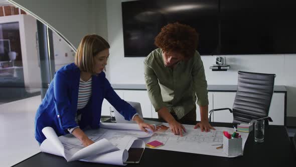 Diverse male and female business colleagues in discussion at work looking at technical drawing