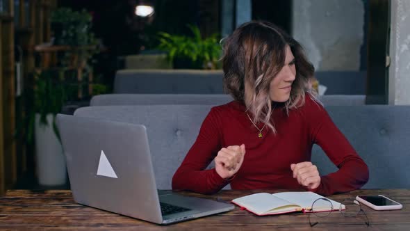 Woman Sitting at a Table with a Laptop and Rejoices