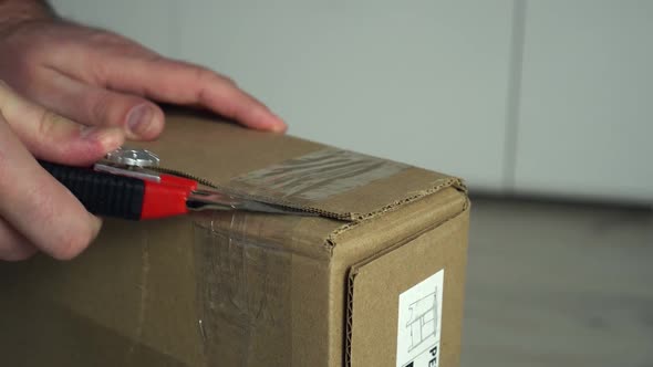 Close Up Mans Hands Open Cardboard Box with Knife at Home Inteerior