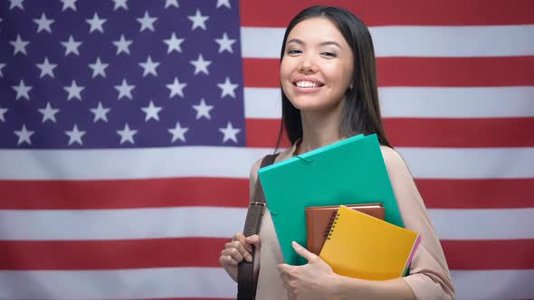 Cheerful Asian Girl Smiling With Books Against USA Flag Background, Education