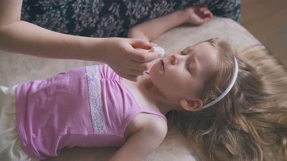 Mother Gives Nose Drops To Little Girl Lying on Soft Bed