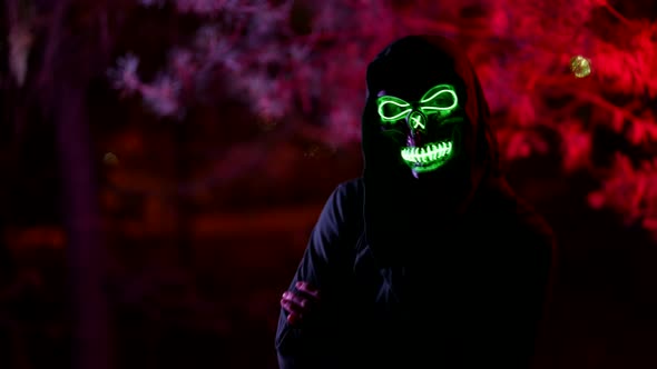 Portrait of a Person in a Terrible Glowing Mask of Death and in a Dark Hood Against the Background