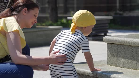 Happy Kid with His Mother Having Fun in Fountain of Public Park at Sunny Summer Day