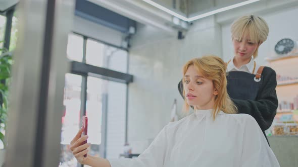 Caucasian woman customer take photo by mobile phone selfie while hairdresser giving service in salon