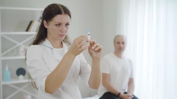 Young Beautiful Woman with Syringe Standing in Hospital Ward with Blurred Stressed Man at the