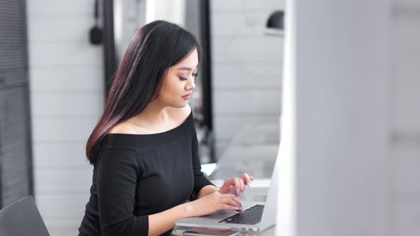 Beautiful Young Asian Businesswoman Typing on Keyboard Using Laptop at Office Side View