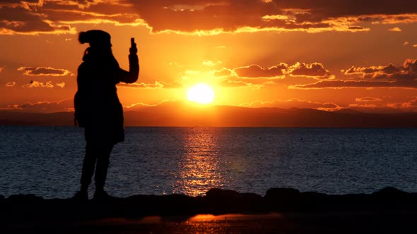 Young Girl Silhouette With Cellphone Near Seaside And Sunset