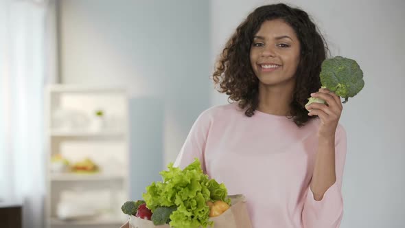 Young Woman Taking Broccoli from Grocery Bag, Smiling at Cam, Healthy Lifestyle