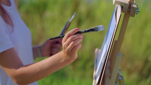 Female Artist is Painting By Blue Dye Landscape Closeup of Easel with Picture