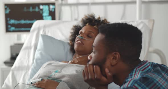 Worried African Husband Sitting at Sick Wife Bed in Hospital