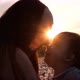 Close Up Silhouette of a Young Woman Kissing Her Young Son Sitting on a Flower Meadow at Sunset - VideoHive Item for Sale
