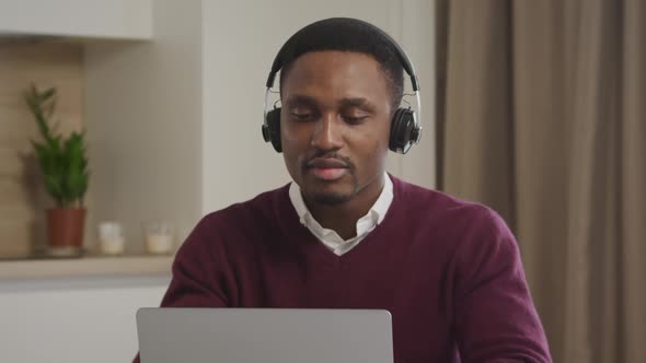 Young Adult African American Man Picks Up Headphones and Starts a Dance in Front of His Laptop