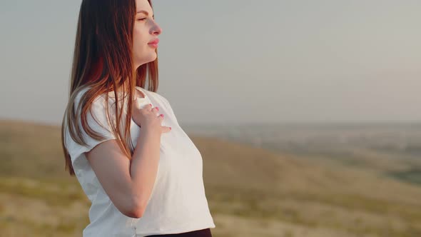 Pregnant Woman Stands on Hill and Performs Breathing Exercises From Yoga with Her Hand on Her Chest