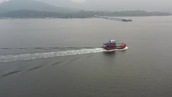 Aerial drone following close to a traditional fishing boat with foamy wake, capturing hard working f