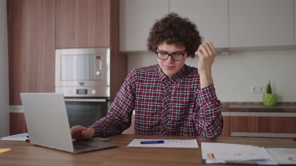 Brooding Serious Curly Freelancer Man Sit at Table in Comfortable Home Office Room Work on Laptop