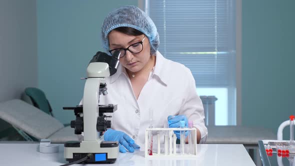 Concentrated Lab Assistant Looks Into Microscope at Table