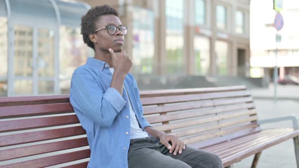 Pensive Young African Man Thinking While Sitting Outdoor on Bench