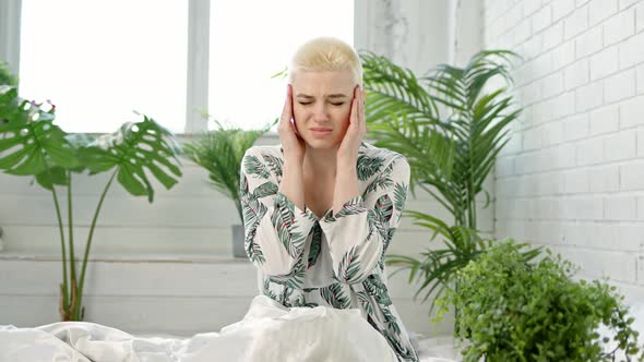 Young Blond Short Hair Woman with Bun on Her Head is Experiencing Severe Headaches