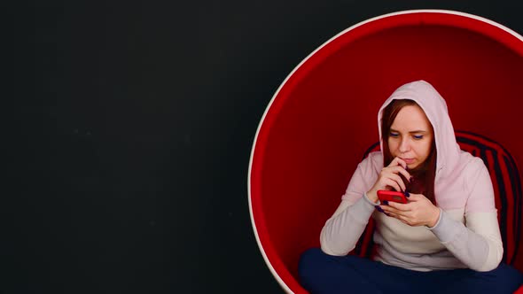 Young Woman with Mobile Phone Sitting in Ball Chair on Black Background