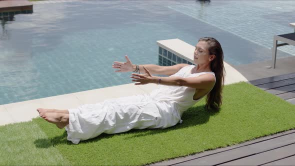 Calm Wpman Practicing Yoga in Balancing Asana Poolside Against Town on Coast