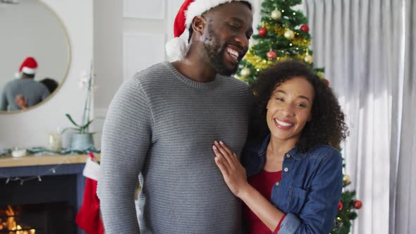 Happy african american couple hugging and looking at camera, christmas decorations in background
