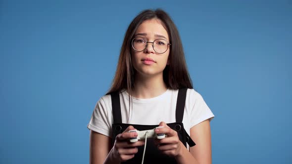 Pretty Asian Girl Playing Video Exciting Game on Tv with Joystick on Blue Studio Wall