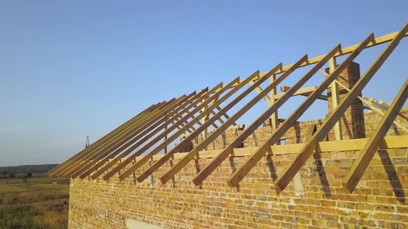 Aerial view of unfinished brick house with wooden roof structure under construction.