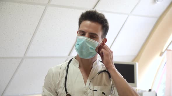 Young Doctor Removes a Medical Mask in Hospital with Ultrasound Devices on Background
