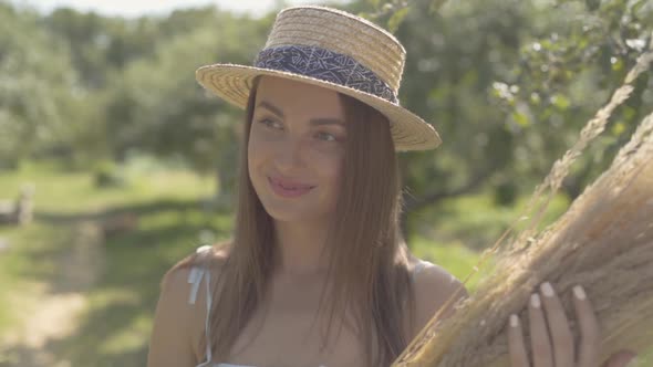 Attractive Young Woman in Straw Hat and Long White Dress Looking at the Camera Smiling Standing in