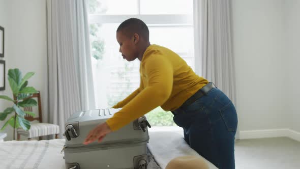 Happy african american plus size woman packing suitcase in bedroom