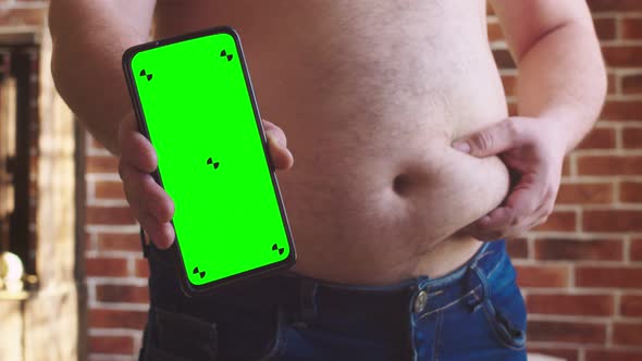 Man Holds Vertically Phone with Chromakey at Level of a Fat Belly with Other Hand Squeezes Full
