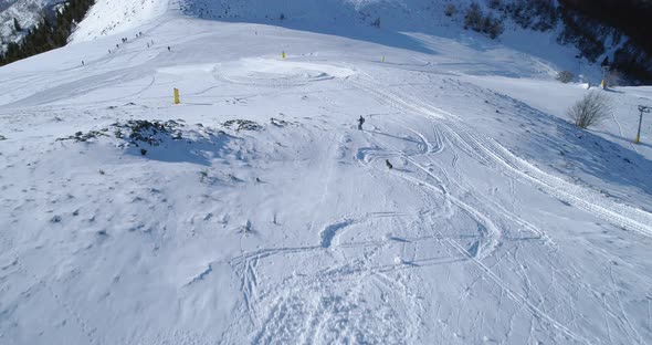 Aerial Follow Over Skier Alpine Skiing with Dog Running Behind in Winter Snowy Mountain Ski Track