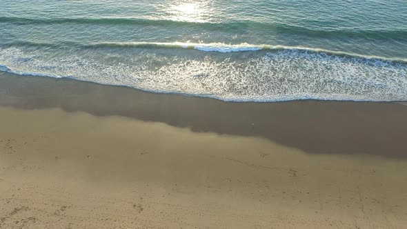 Aerial shot of the sun setting over a beach and ocean horizon.