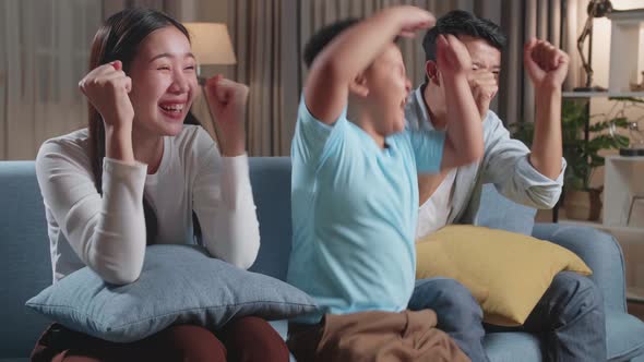 Asian Family Celebrating While Watching Tv Together Sitting On A Sofa In The Living Room At Home