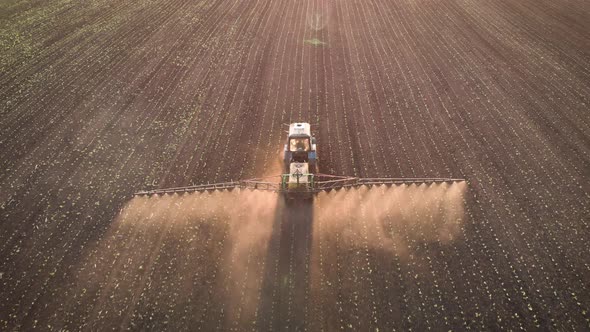 Aerial View of Farming Tractor Spraying on Field with Sprayer, Herbicides and Pesticides at Sunset