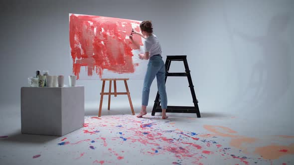 Back View Woman Artist Draws with a Brush on a Large Canvas in a White Room a Talented Artist Draws