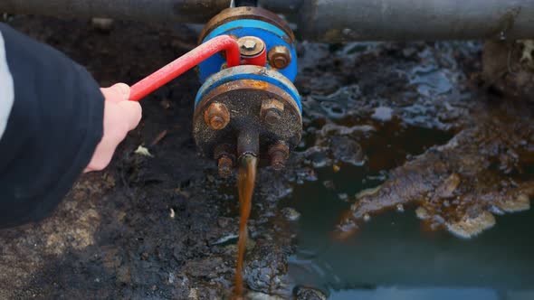 An Oil and Gas Worker Opens a Tap From a Pipe and Crude Oil Begins to Flow to the Ground