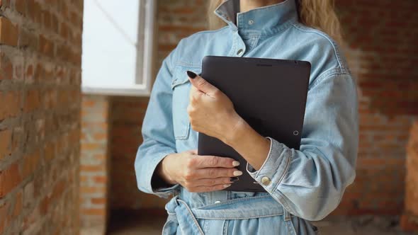 A Female Architect or Bricklayer Stands in a Newly Built House with Untreated Walls with a Tablet in